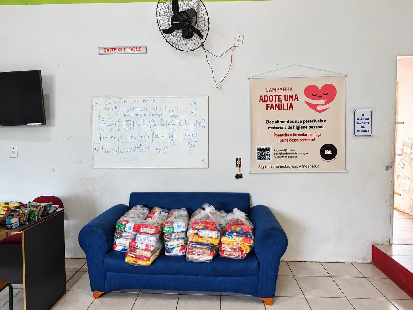 Cestas básicas organizadas para distribuição, ao lado do banner da campanha Adote uma Família.