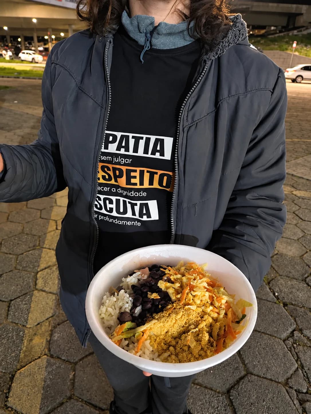 Pessoa segurando uma marmita com refeição quente entregue pelo Nós na Rua durante a ação noturna.